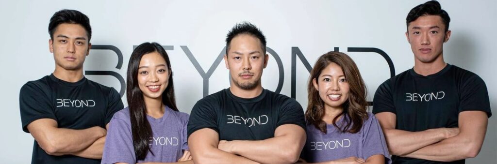 Group of five fitness coaches wearing Beyond shirts, standing with arms crossed for a team portrait.