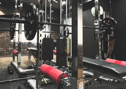 Weightlifting area with a barbell on a squat rack, loaded with plates, and a bench with red padding.