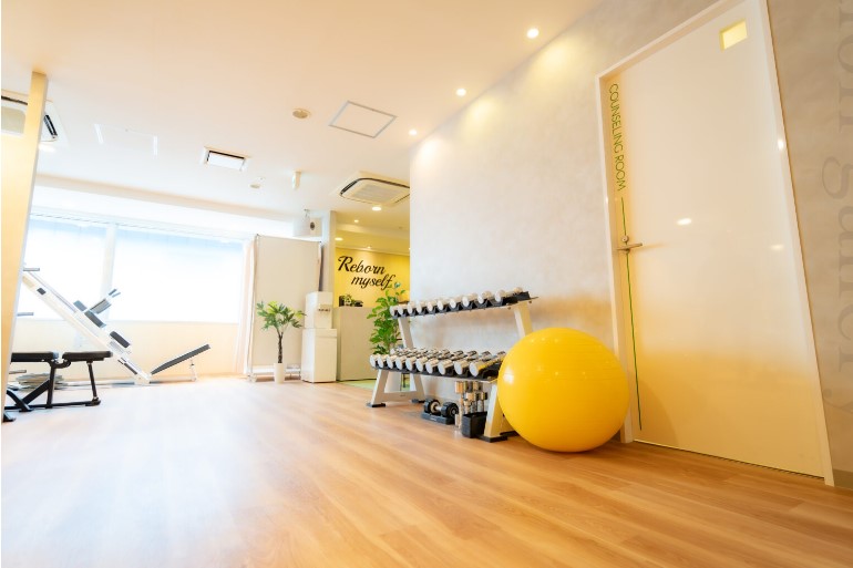 Bright fitness studio with a rack of dumbbells, a large yellow exercise ball, and a wooden floor in natural light.